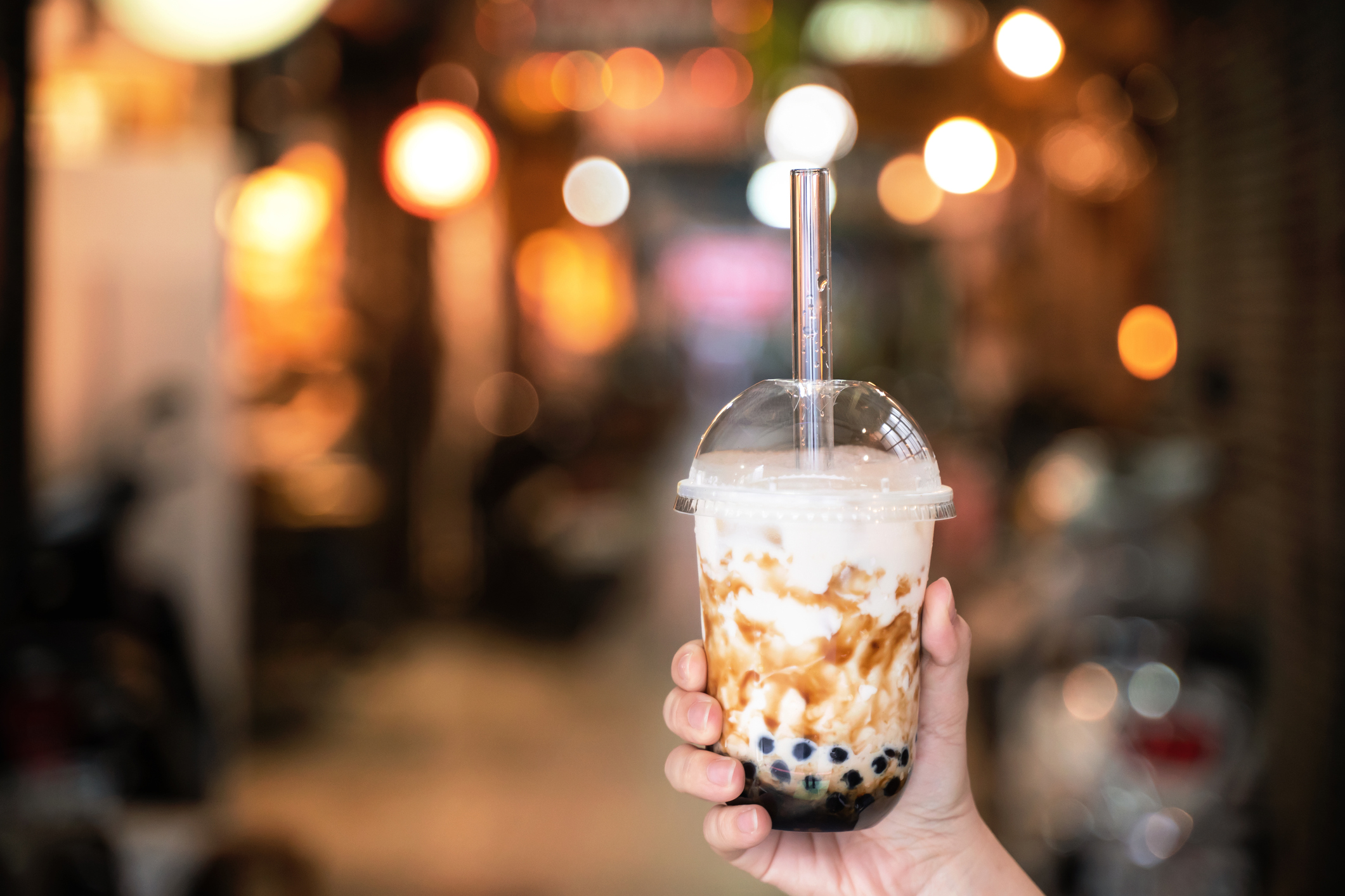 Young girl in denim jacket is drinking brown sugar flavored tapioca pearl bubble milk tea with glass straw in night market of Taiwan.